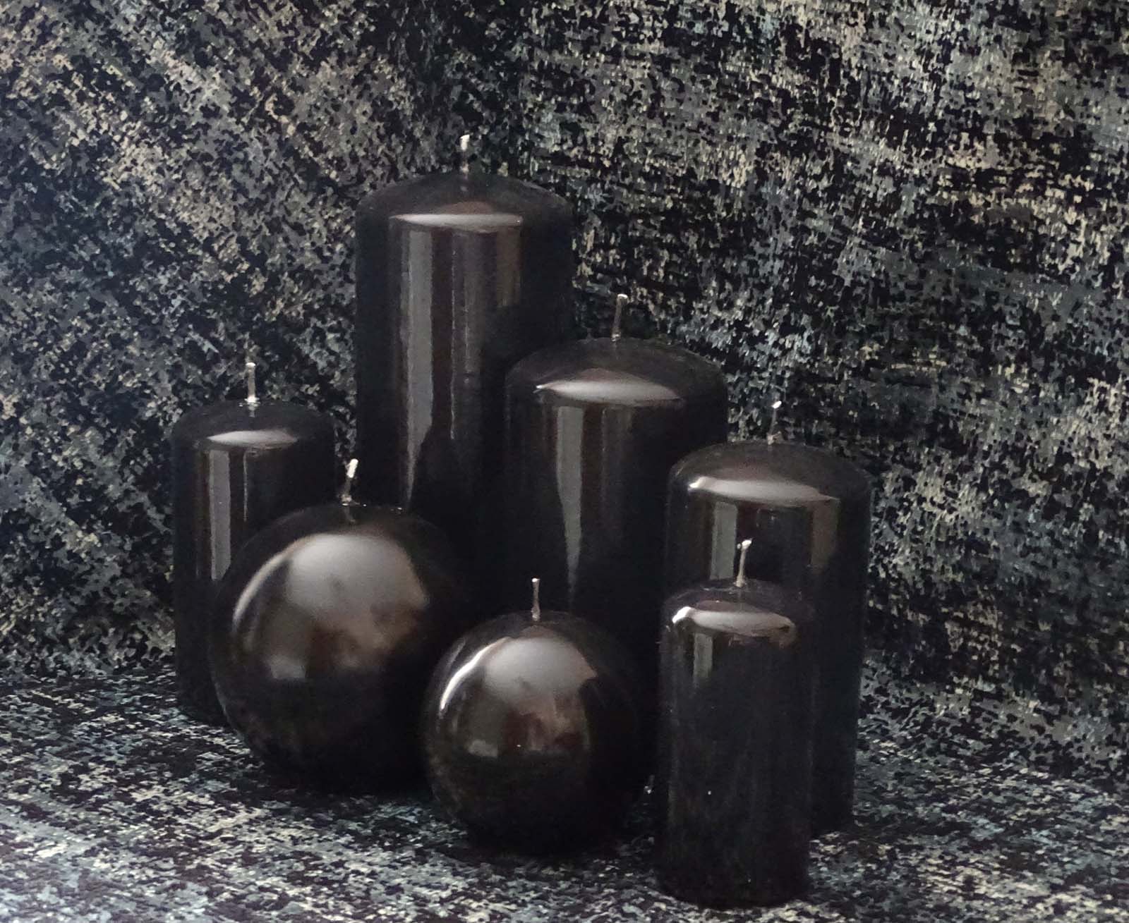 Five pillar and two round black gloss candles sitting on the black and gray cloth
