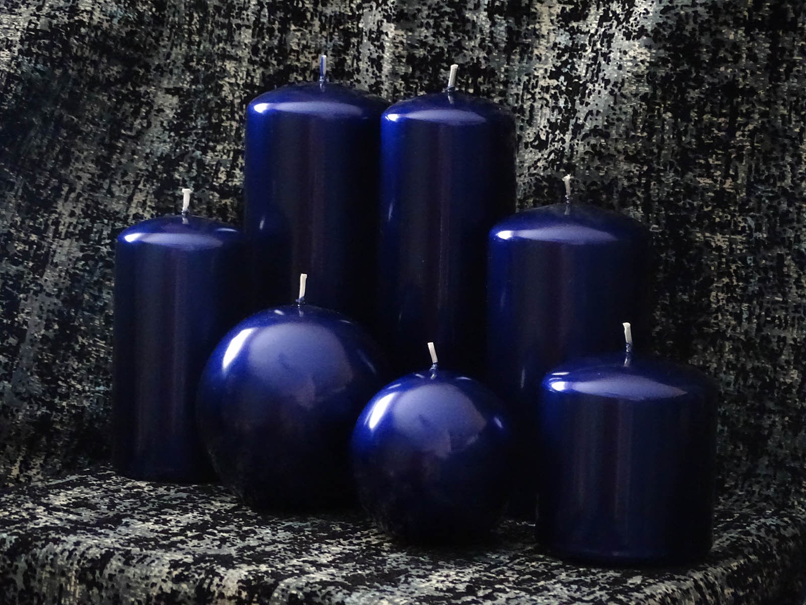 Five pillar and two round navy blue candles on the dark background 