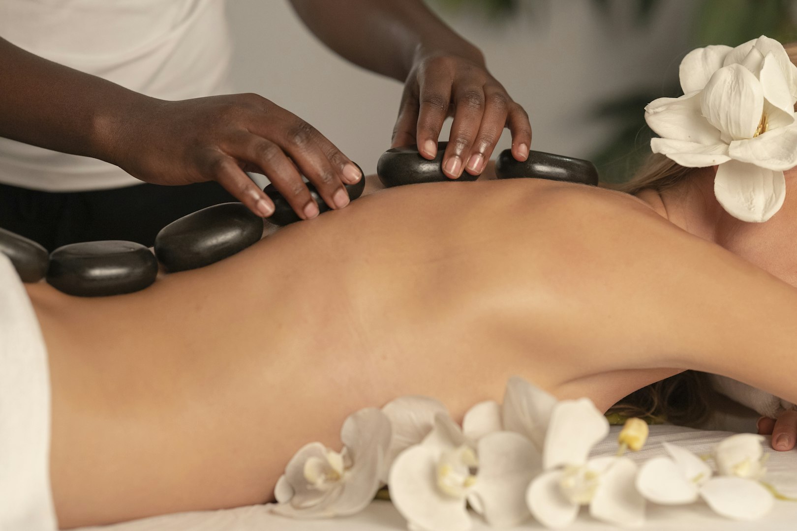 Woman lying on the massaging bead and massage therapist is placing stones on patients back